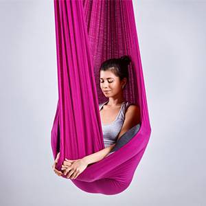 Frau mit Aerial Yoga Tuch bei der Ausführung einer Aerial Yoga Figur